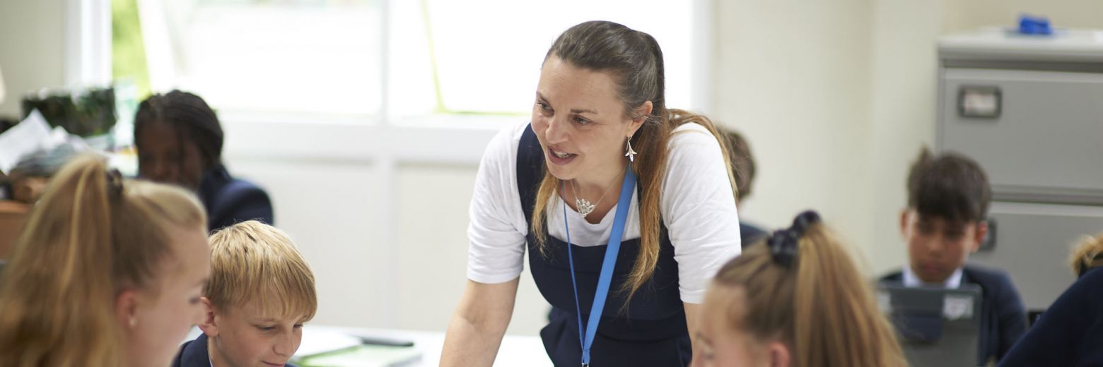 teacher leaning over a desk to talk to students