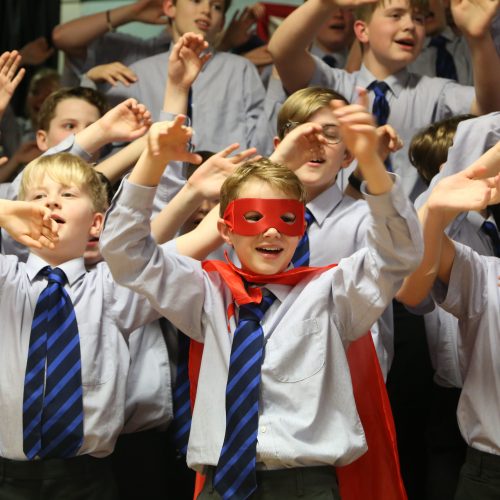 children in a crowd singing with their arms in the air